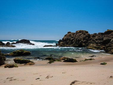 Portekiz 'in kumlu sahillerinde kayalar açık mavi su ve bulutsuz gökyüzü ile güneşli bir yaz gününde