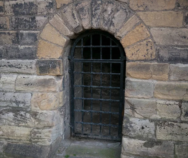 Arched entrance to an old. medieval , stone castle dungeon in Northern England with iron bars