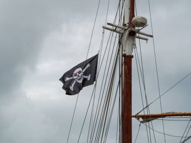 Jolly Roger / Korsan bayrağı Bir yelkenli gemisinin direğinden dalgalanan kafatası ve çapraz kemikler.