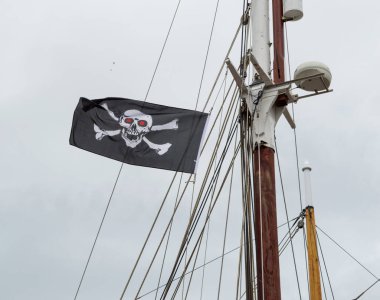 Jolly Roger / Korsan bayrağı Bir yelkenli gemisinin direğinden dalgalanan kafatası ve çapraz kemikler.