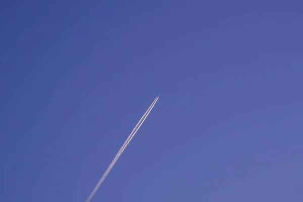 Jet airliner plane flying at high altitude leaves vapor trail / contrail against dark blue sky