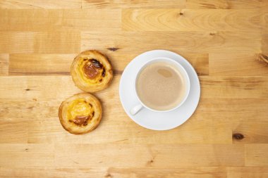 Kahve fincanı ve pastel de nata olarak bilinen Portekiz kremalı tartları. Tahta masanın üstünden aşağı doğru..