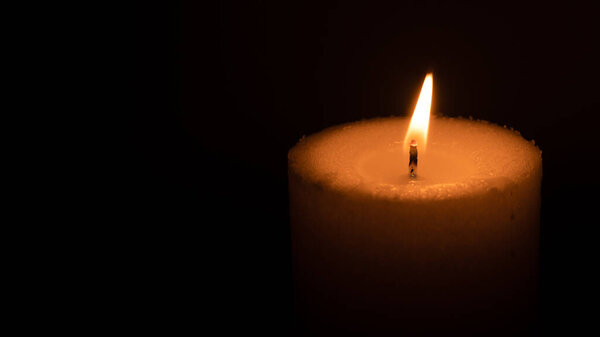 Candle burning in the dark with copy space on left