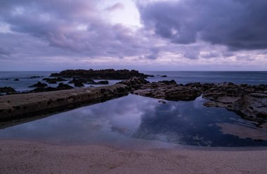 Gökyüzü alacakaranlıkta sahildeki kaya havuzuna yansıyor. Uzun pozlama.