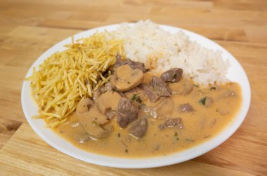 Tipik Brezilya Stroganoff tabağı. Beyaz tabakta patates çubukları ve pirinç ve ahşap masa..