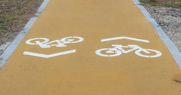 Cycle path with two lanes, and directions marked on the ground. Yellow asphalt and white bicycles painted.