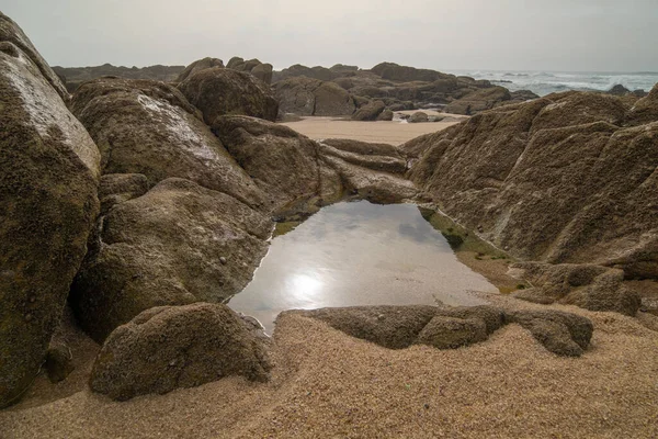 Rock pool formed between rocks on the beach, with sun reflected on water surface