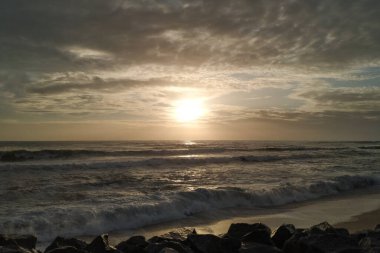 Portekiz sahillerinde gün batımında karanlık, dramatik bulutlar ve siluette kayalar.