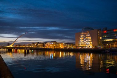 Dublin, İrlanda şehri geceleri Liffey nehri üzerinde. Suya yansıyan ışıklarla Kongre Merkezi ve Samuel Beckett Köprüsü / Harp Köprüsü