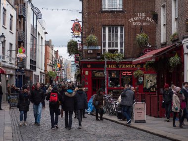 Turistler ve ziyaretçiler İrlanda 'nın Dublin kentindeki Temple Bar bölgesindeki renkli İrlanda barlarının önünden geçerek kaldırımlı yolda yürüyorlar..