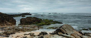 Kayalık sahilde, dramatik bulutlar ve kışın karamsar gökyüzü. Uzun pozlama