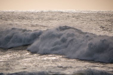 Büyük, güçlü beyaz dalgalar alacakaranlıkta yumuşak altın ışıkla dalgalanır.