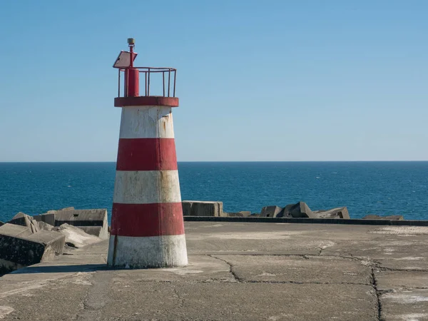 Red and white light house at end of harbour wall in Povoa de Varzim, Portugal, with ocean in background