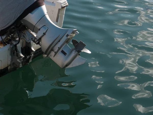 Outboard motor with propellor out of water, on the back of a small boat in water