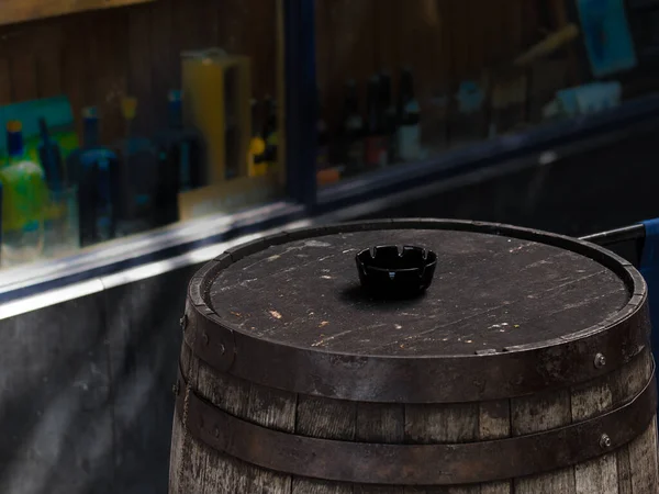 Old whiskey barrel with a black ashtray outside pub in Dublin Ireland, with bottles in window.