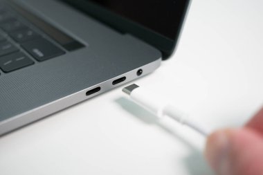 Gri bir dizüstü bilgisayar / dizüstü bilgisayar üzerinde beyaz bir USB-C / Tip C kablosunu bir porta takmak.