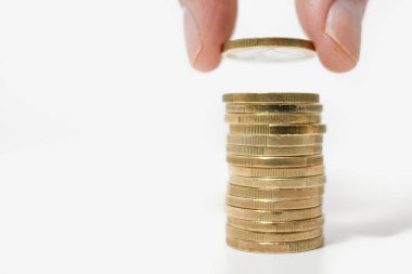 Beyaz bir masanın üzerine, parmakla başparmak arasında duran bir yığın altın Euro sikke inşa etmek. Boşluğu sola kopyala.