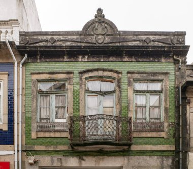 Porto, Portekiz 'deki eski Portekiz mimarlık binasının geleneksel cephesi. Yeşil kiremitleri ve metal balkonu var. Yıpranmış, kırık camlar.. 