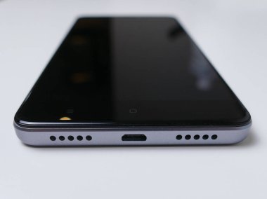 Beyaz masa arkasında modern bir cep telefonu. Mikro USB portunu gösteren alt görünüm. Siyah ve gümüş / alüminyum.