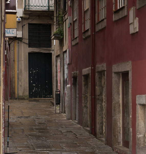 Narrow street in Porto, Portugal with traditional Portuguese architecture and old stone door frames. Wet ground on a rainy day.