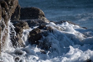 Okyanus kıyısındaki kayaların üzerinden süzülen köpüklü beyaz dalgalara yakın.