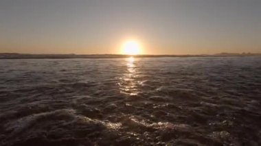 Yazın gün batımında, dalgalar kameraya doğru akın ediyor ve kameraya doğru sıçrıyor..