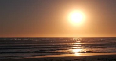 Yazın gün batımında güzel kumlu sahil. Ufkun üzerindeki güneş ve suyun üzerindeki yansımalar. Geniş açı görünümü, sağda güneş var..
