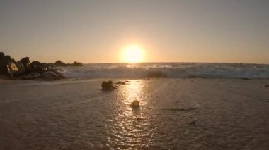 Alçak açı dalgaları yazın günbatımında kumlu sahil şeridini silip süpürüyor. Yavaş çekim.