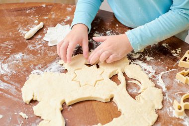 Çocuk beyaz arka plandaki masada hamurdan kurabiye yapıyor.