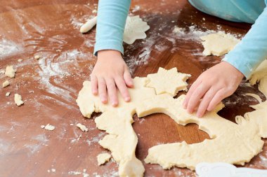 Çocuk beyaz arka plandaki masada hamurdan kurabiye yapıyor.