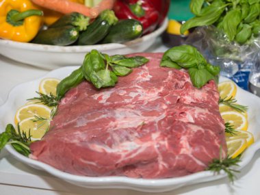 Bir dilim limon ve fesleğen ve biberiye ile süslenmiş bir tabakta ham sığır eti