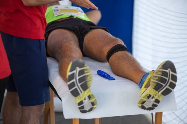 Atleta deitado em uma cama enquanto tem pernas massageadas após um treino de esportes físicos — Fotografia de Stock