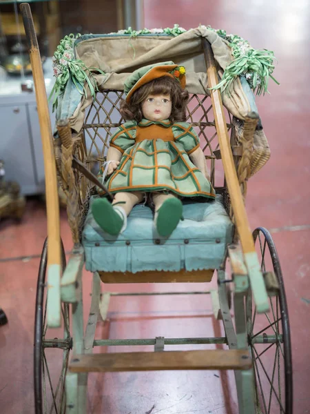 Bambola antica con abito verde e arancione poggiante su un passeggino in legno e vimini — Foto Stock