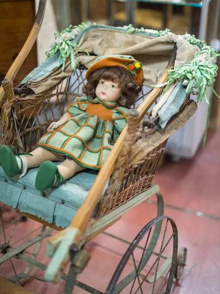 Antique Doll with Green and Orange Dress Resting on a Wooden and Wicker Stroller — Stock Photo, Image