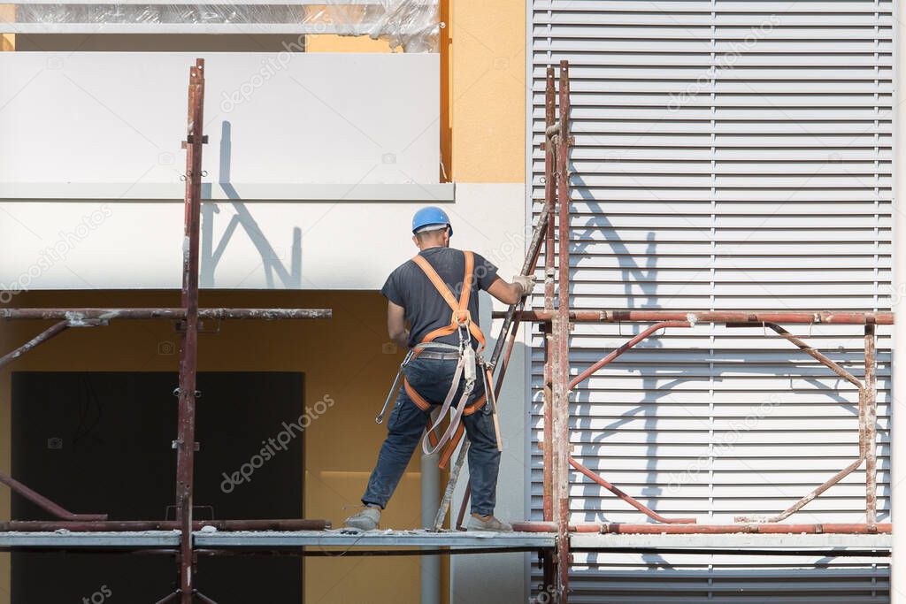 Worker with Blue Hardhat at Work on a Scaffold in a Building Site for the Construction of a Building.