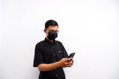 Maskeli genç bir Asyalı telefonuyla mesaj yazıyor.