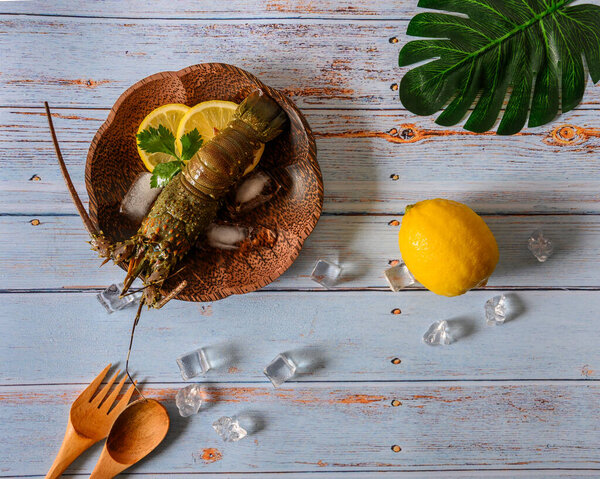 Raw fresh seafood lobster preparation for cooking complete with yellow lemon and ice cube on glass tray and blue old texture table