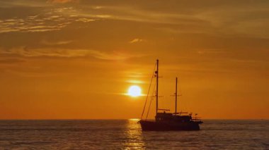 Turuncu gün batımında yelkenli denizde süzülür.