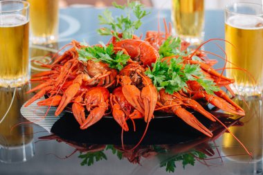 Kaynamış kerevit siyah tabakta masada, bira bardaklarının yanında.