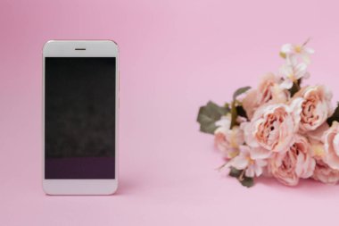 Arka planda çiçekler olan pembe arka planda cep telefonu.