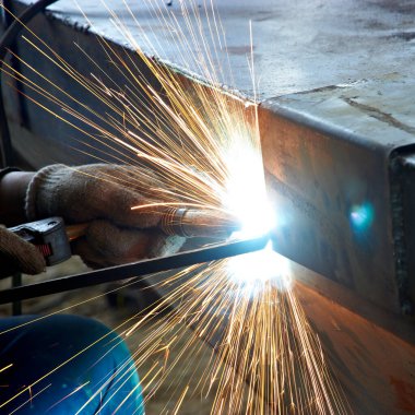 İşçi atölyede kaynak yaparken kaynaktan kıvılcımlar çıkıyor.