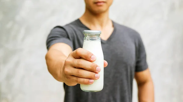 Elinde gri arka planda bir şişe süt tutan adam..