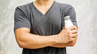 Elinde gri arka planda bir şişe süt tutan adam..