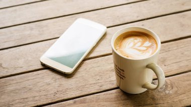 Sıcak latte kahve ve ahşap masada akıllı telefon..
