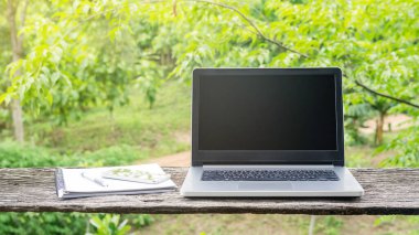 Laptop, akıllı telefon, kalem ve kitap ahşap bir masada..