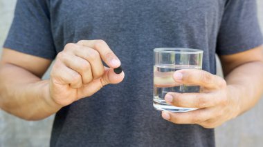 Elinde aktif kömür hapları ve bir bardak su tutan bir adam..