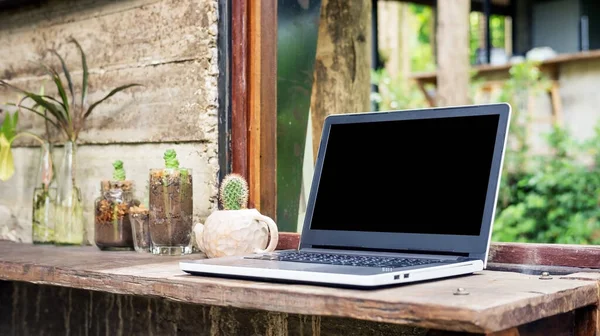 Bir pencerenin yanında dizüstü bilgisayar ve kaktüs.