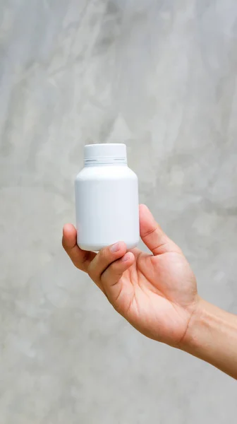 Gri arka planda beyaz bir ilaç kasesi tutan adam..