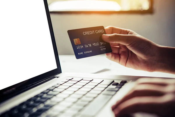 Hand holding a credit card in their hands and find information about a product using their mobile device to make purchases online and conduct financial transactions.