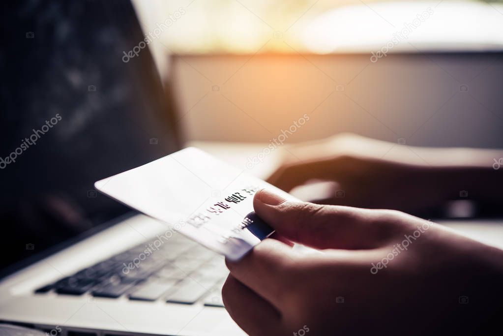 Hand holding a credit card in their hands and find information about a product using their mobile device to make purchases online and conduct financial transactions.